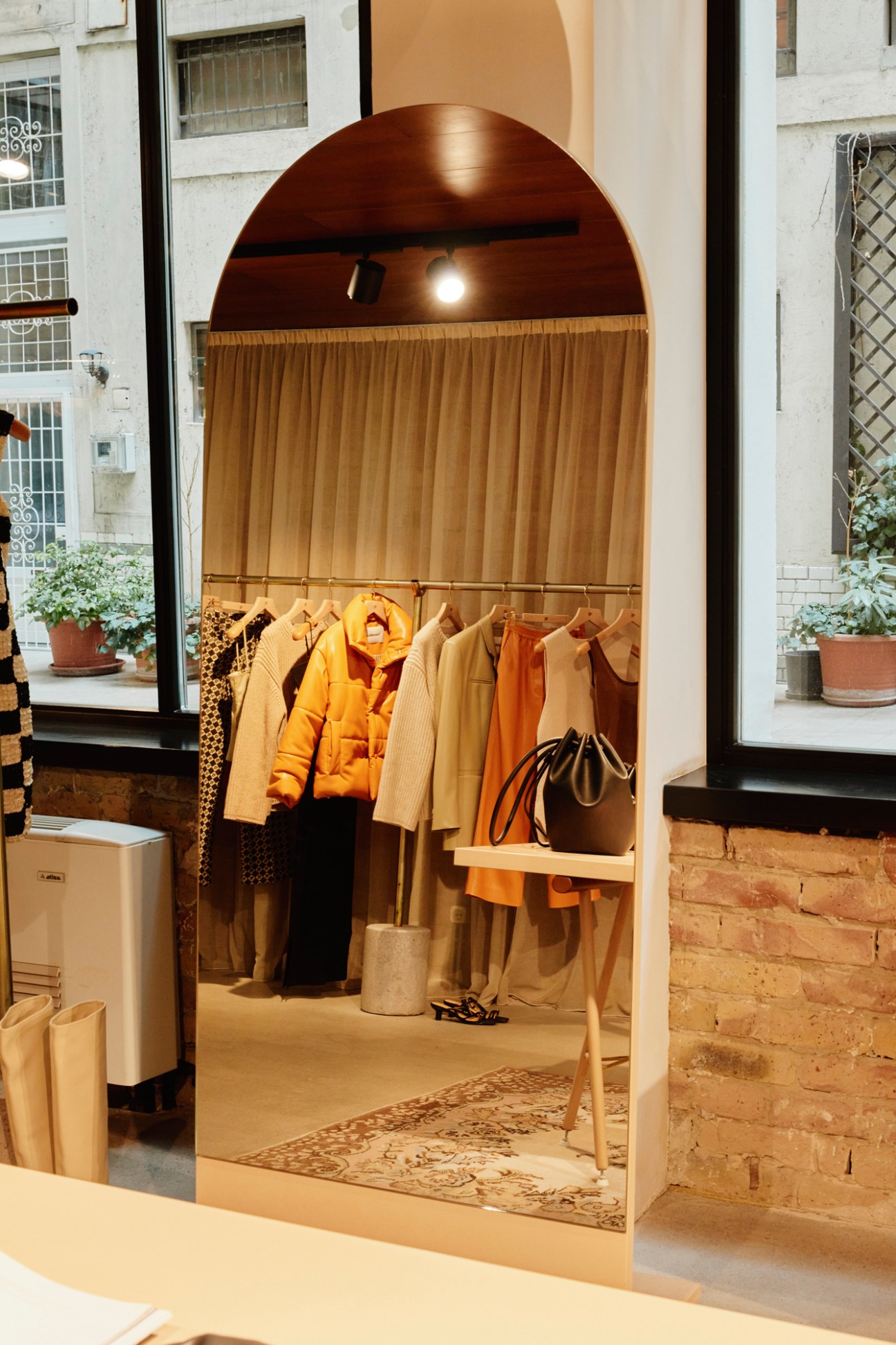 Interior of a boutique clothing store with an arched alcove displaying hanging garments in neutral tones