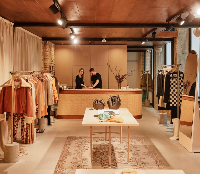 Interior of Nanushka shop in Budapest with clothing racks, central display table, and two staff members at counter