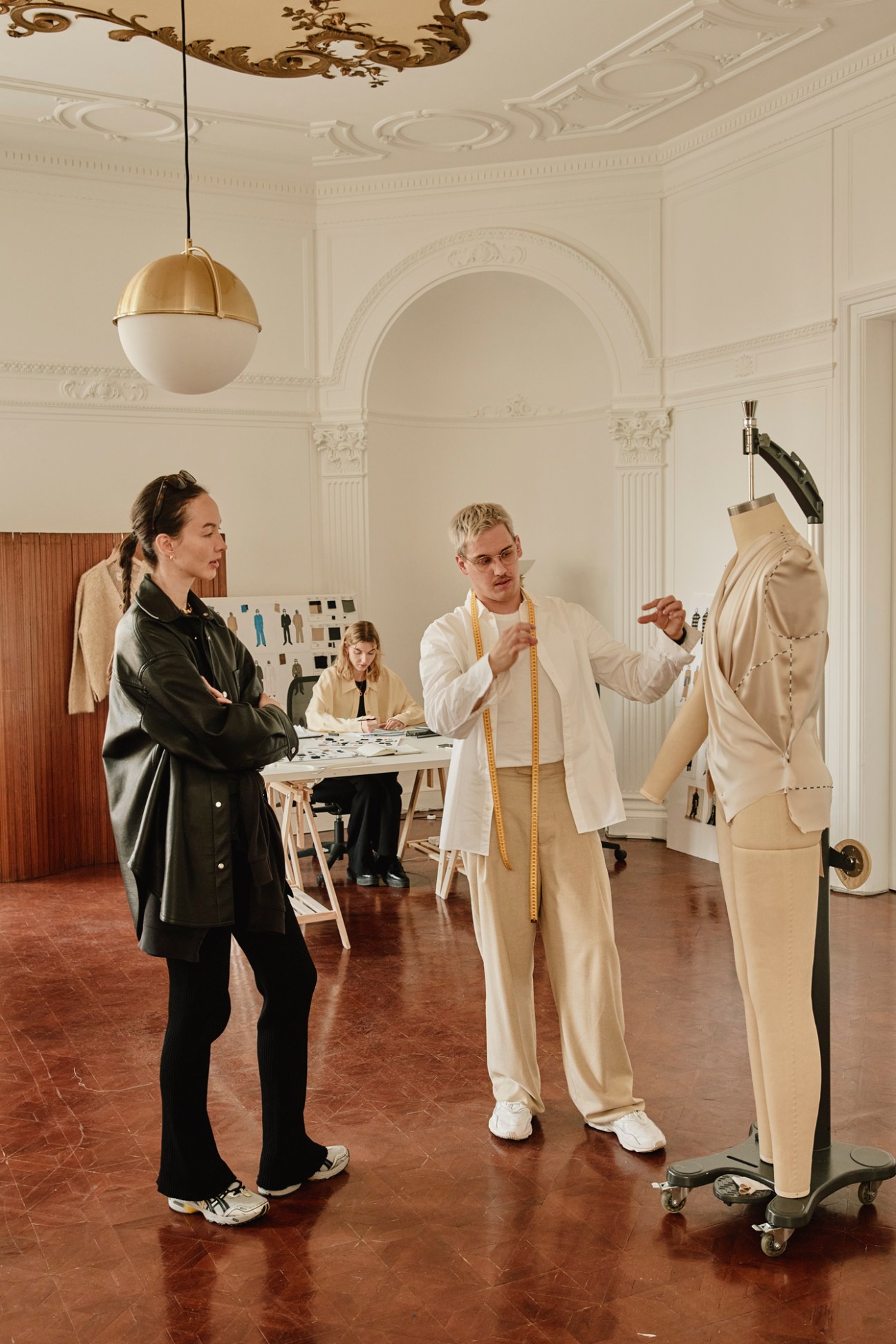 Two people working in a fashion design studio with dress form and fitting in progress