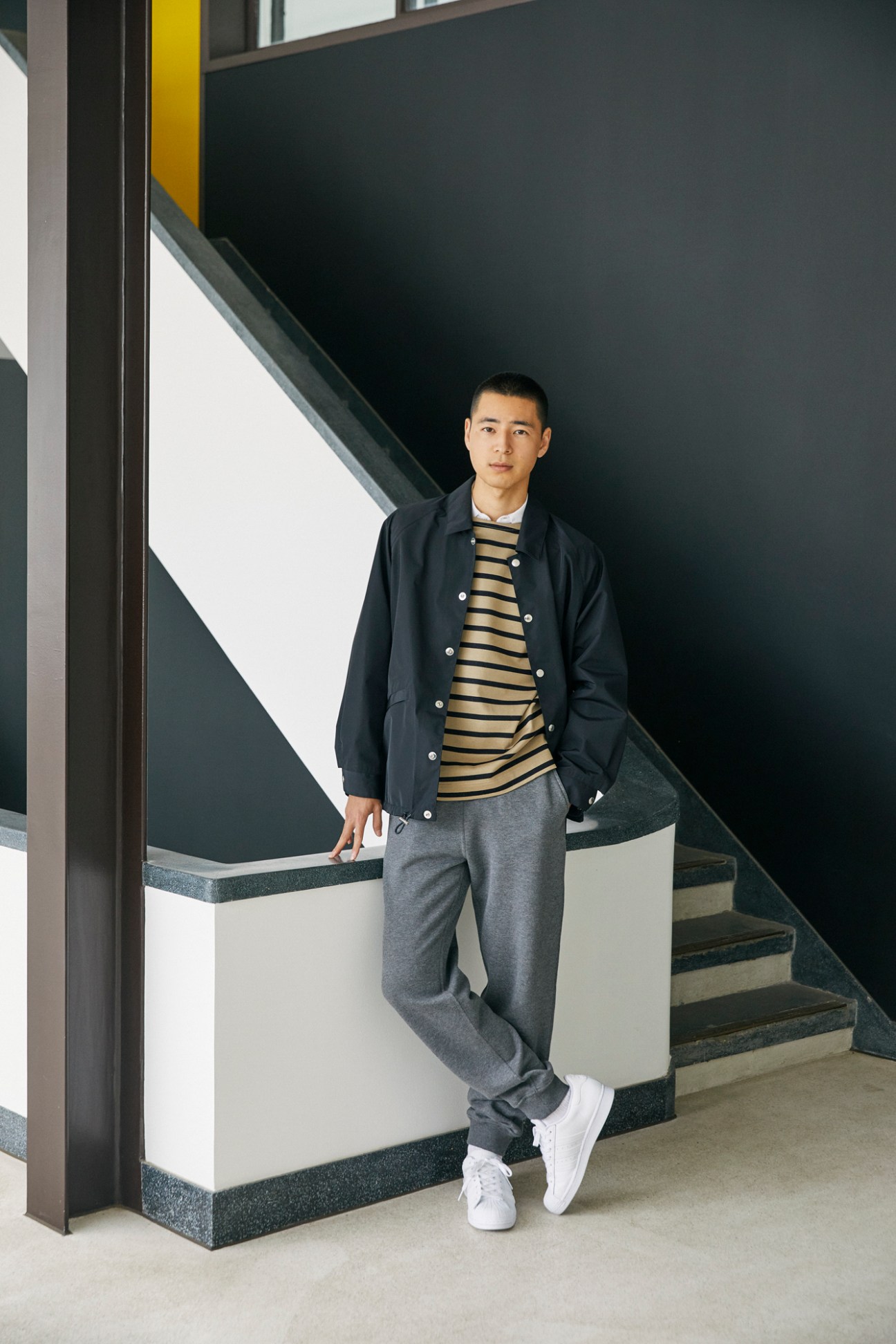 Man in navy jacket and striped jumper posing on modern staircase in contemporary interior