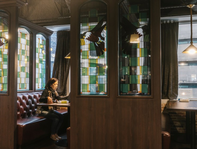 Woman reading in a leather booth beside green stained glass windows.