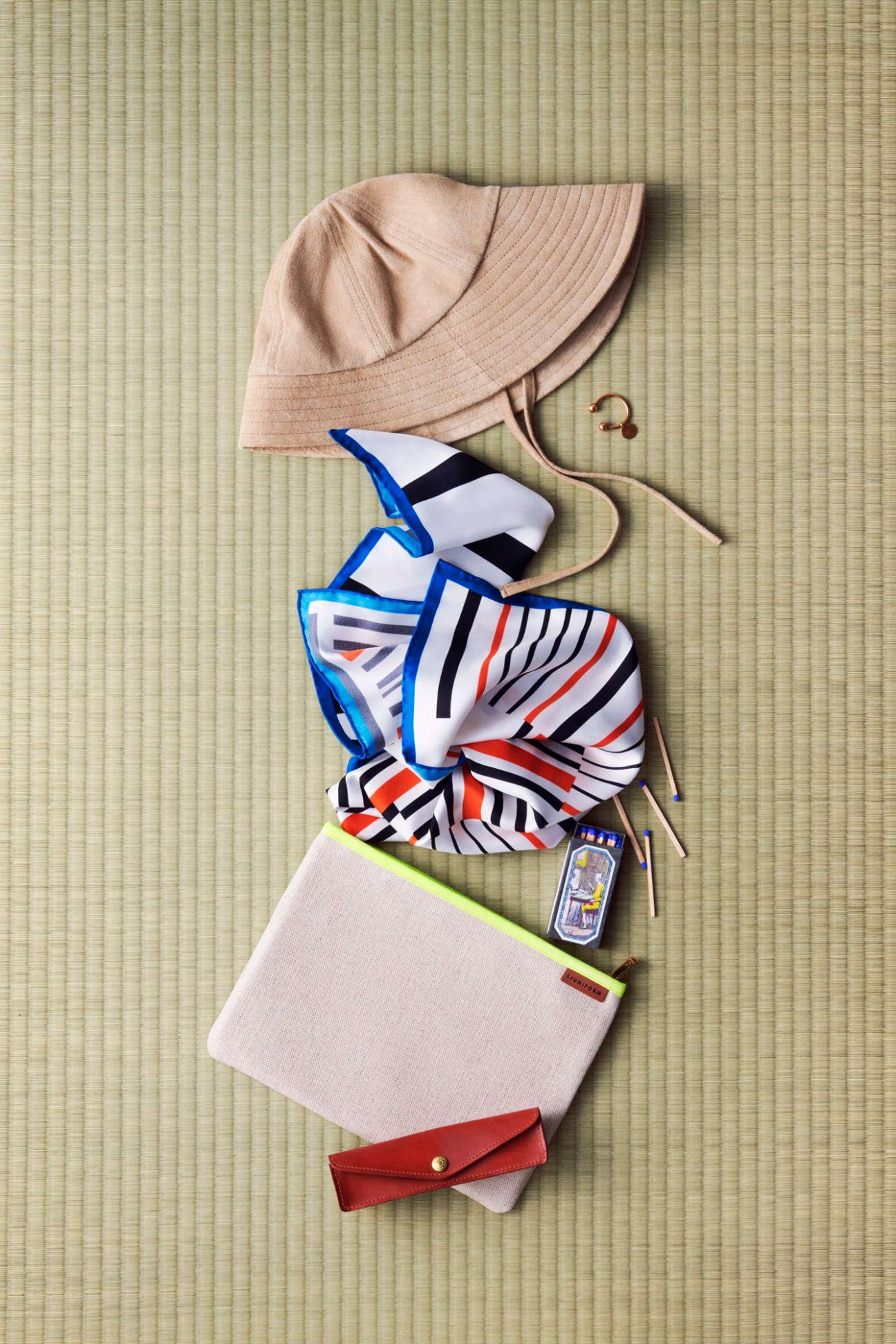 Hat, striped scarf, canvas bag, and leather pen case arranged on woven mat surface