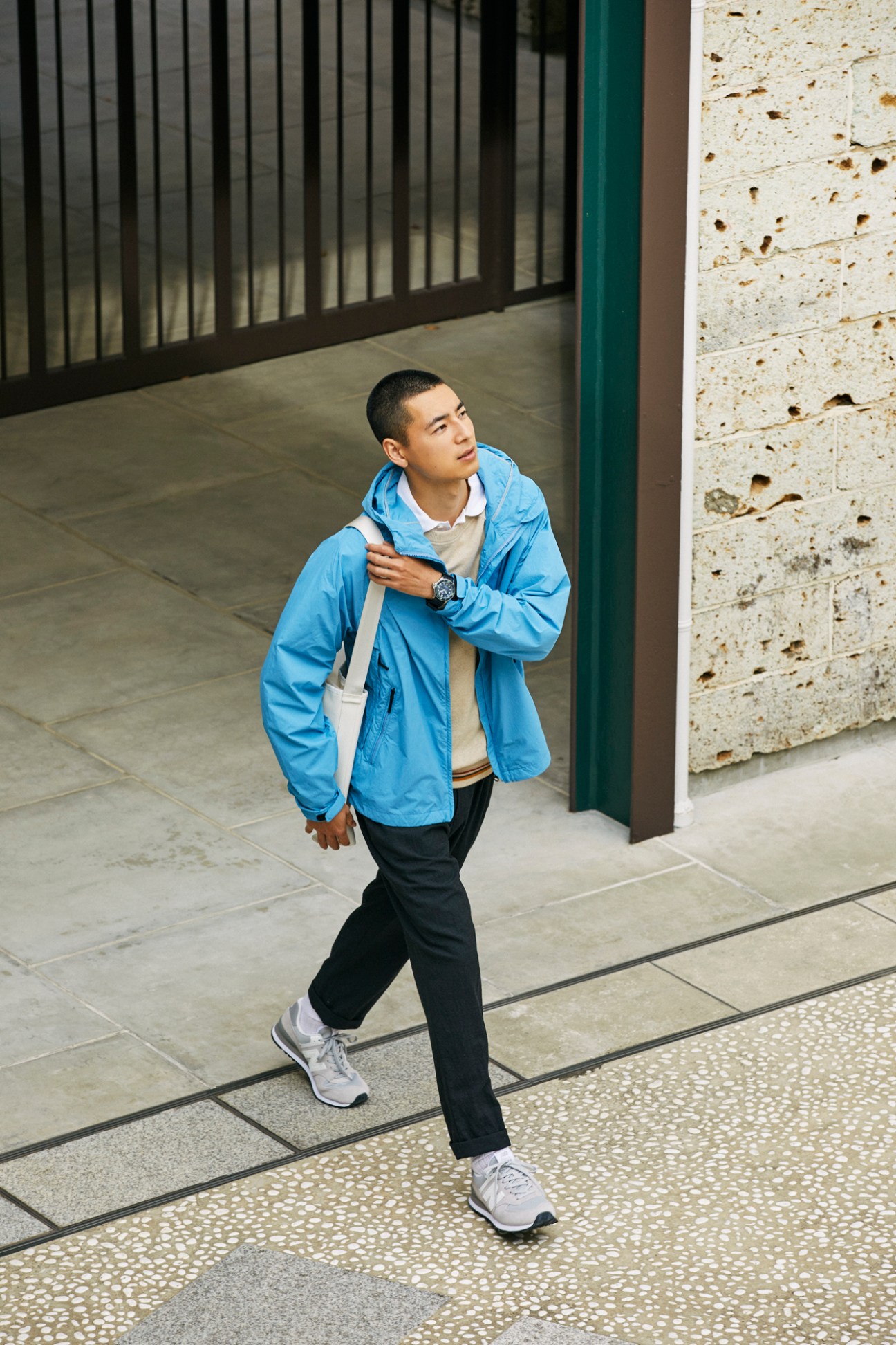 Man in light blue jacket and dark trousers walking through modern courtyard with geometric paving
