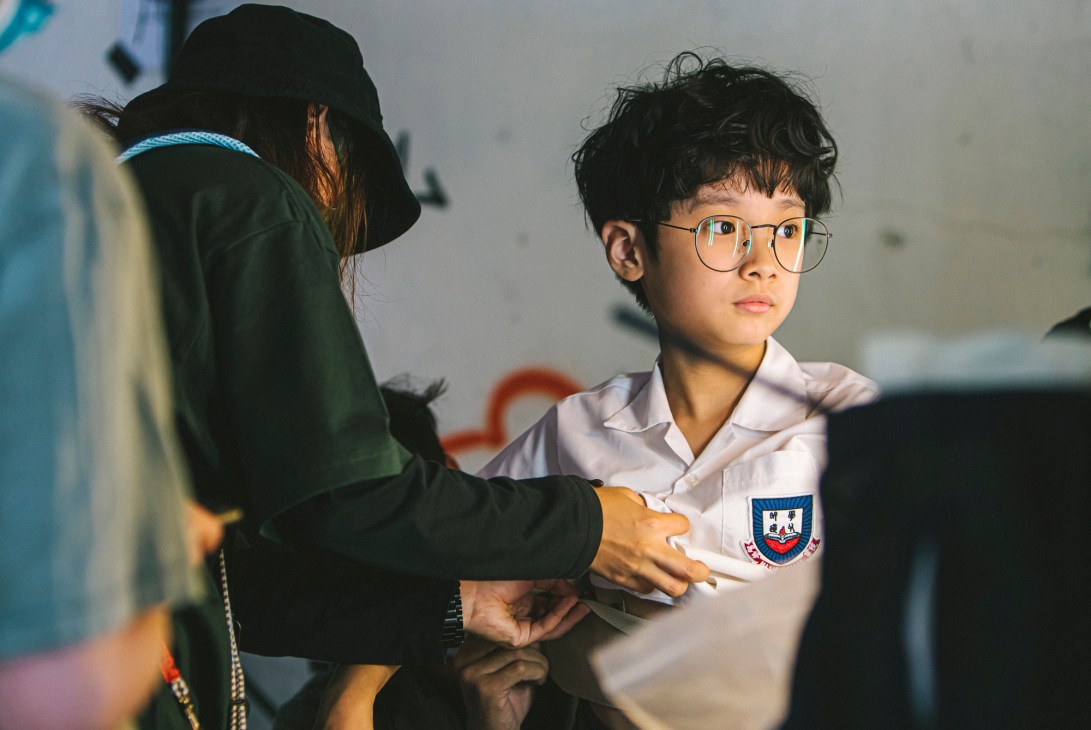 Young person in white school uniform with school crest being fitted or measured by someone in dark clothing