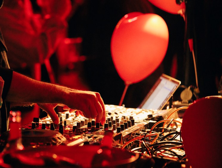 DJ's hands on turntables under red stage lighting at Nåpoleon Komplex nightclub.