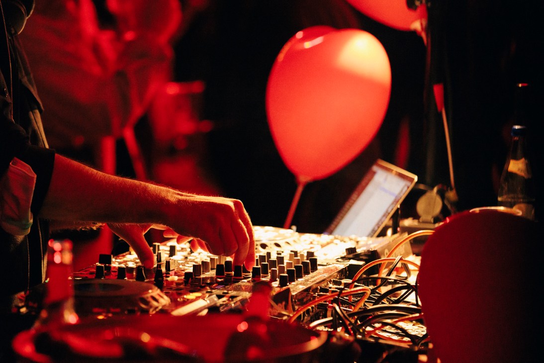 DJ's hands on turntables under red stage lighting at Nåpoleon Komplex nightclub.