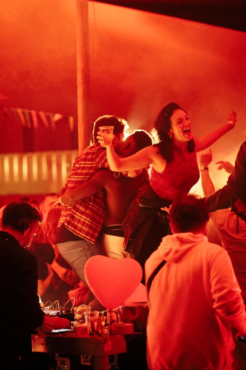 People dancing and celebrating at Nåpoleon Komplex nightclub in Berlin with warm red lighting.