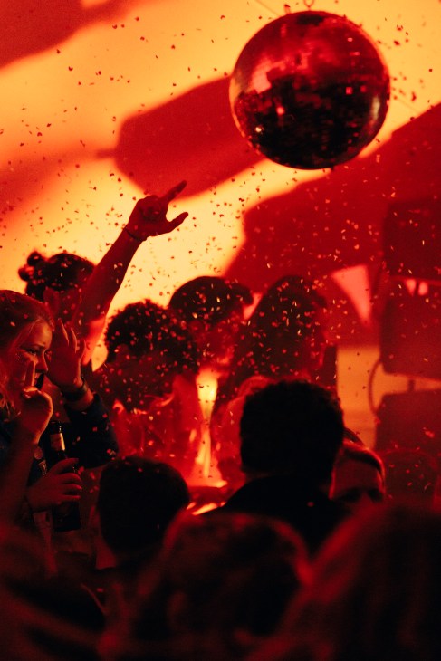 Revellers dancing under red and orange lighting with a glowing ball at Nåpoleon Komplex nightclub in Berlin.