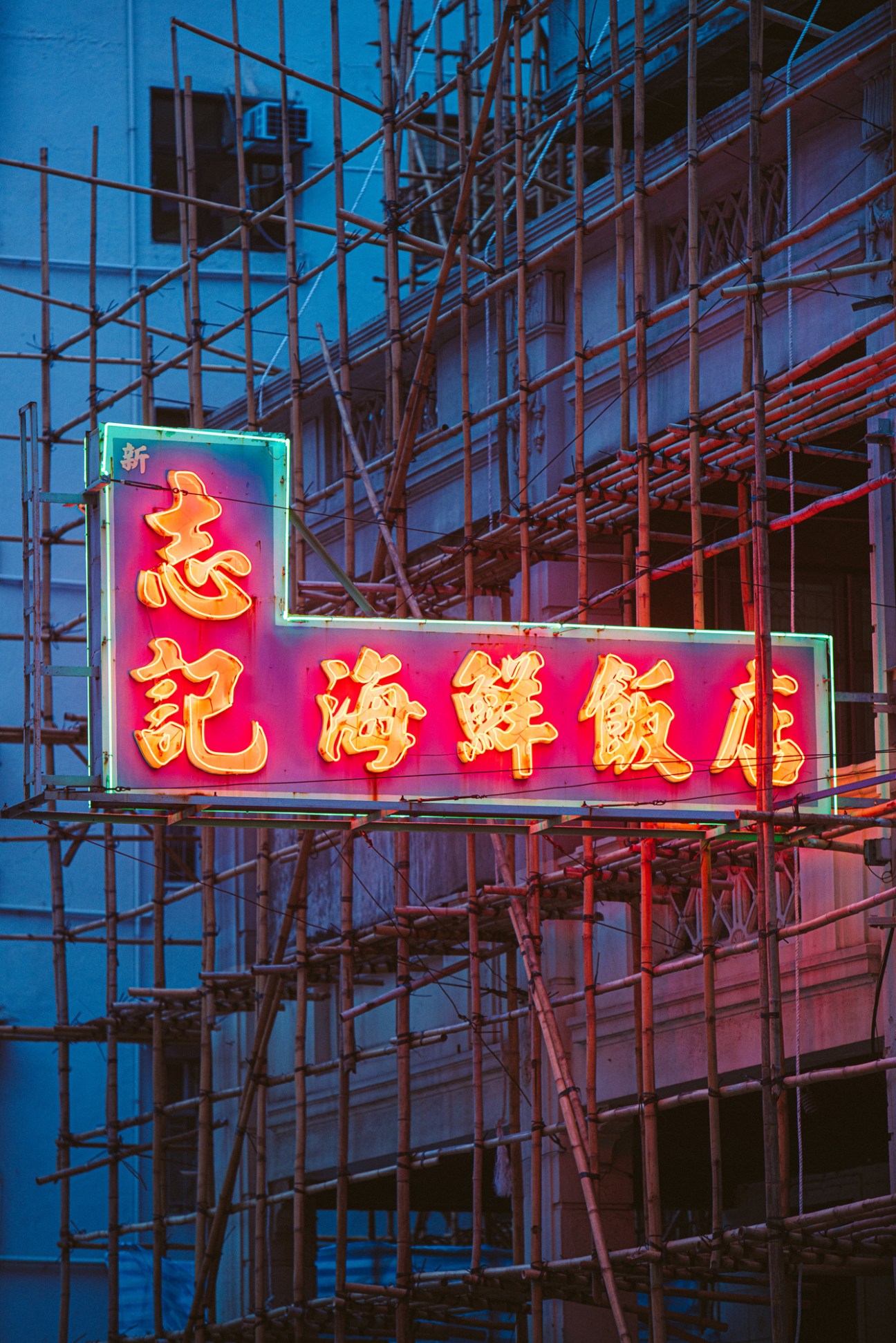 Neon sign with Chinese characters in red and yellow on pink background surrounded by construction scaffolding