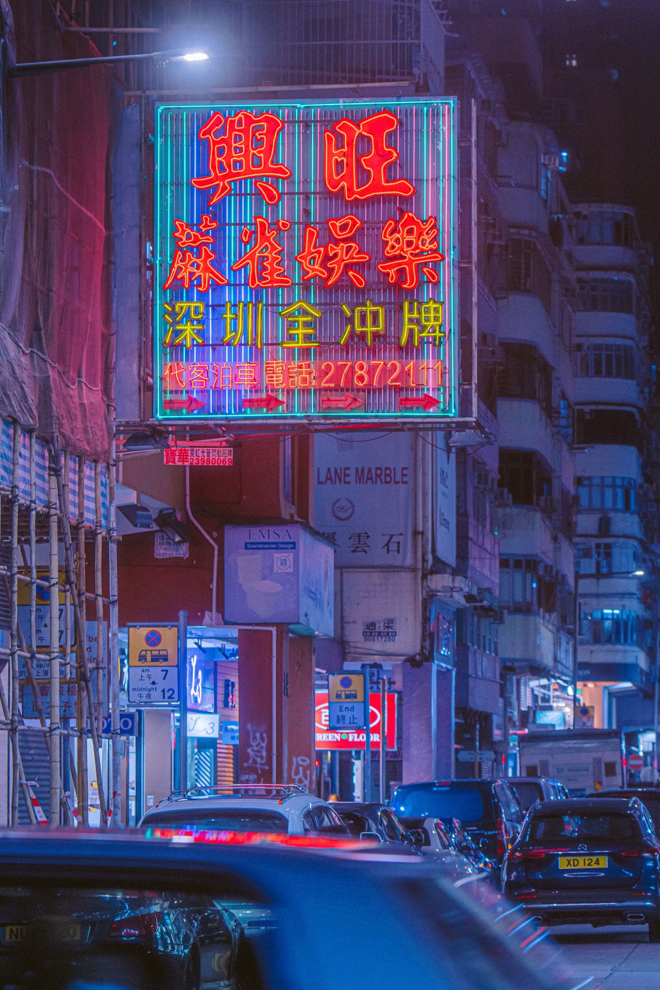 Neon signs with Chinese characters in red and yellow illuminate a Hong Kong street at night with cars parked below