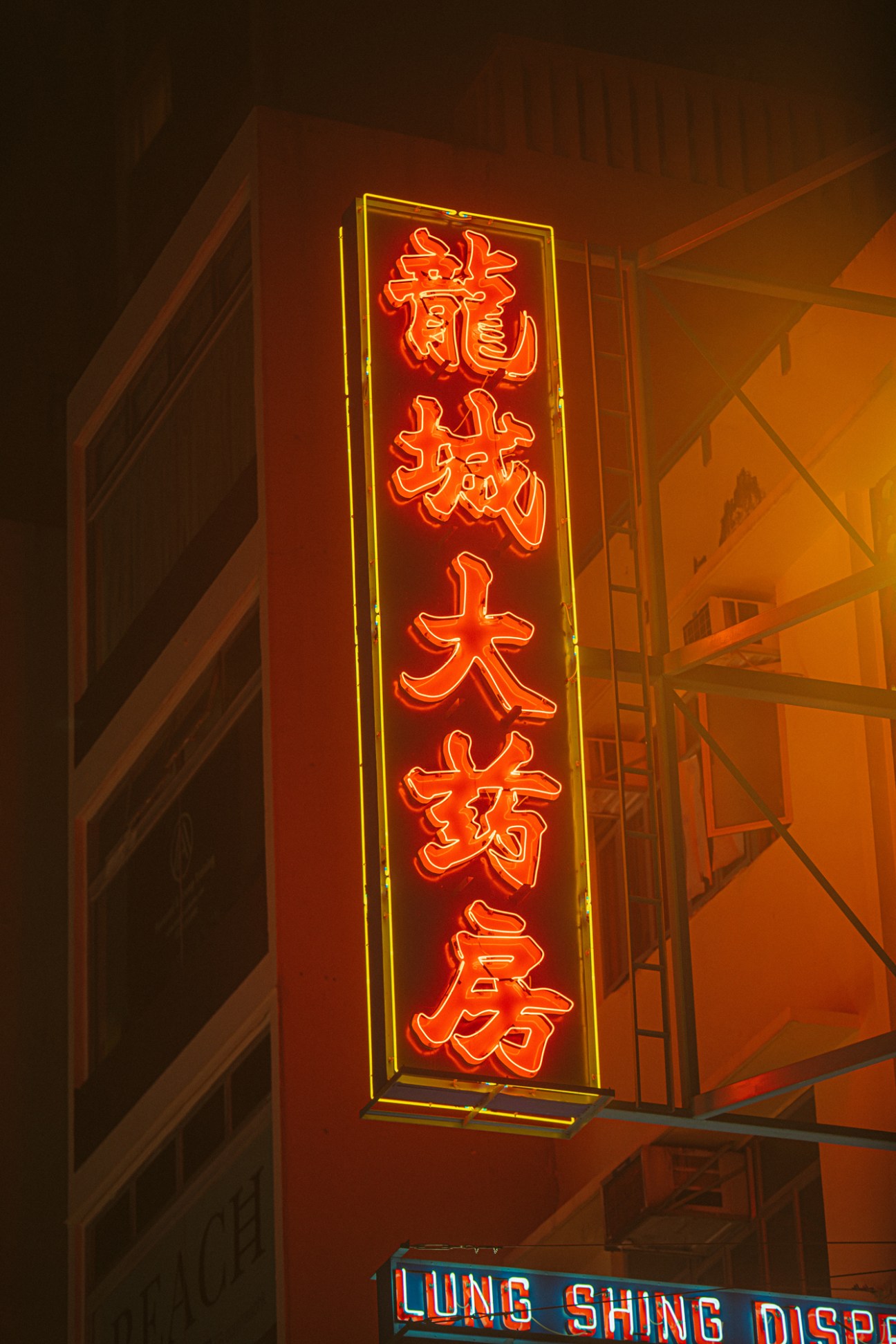 Vertical red neon pharmacy sign with Chinese characters and yellow border mounted on building corner