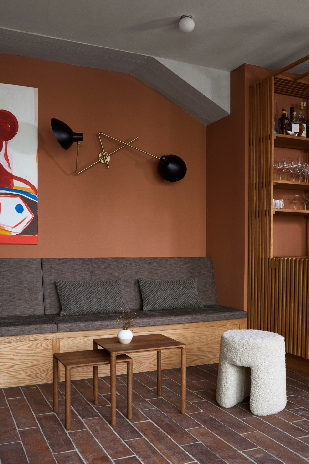 Modern restaurant interior with gray banquette seating, warm brown walls, artistic lighting, and wooden shelving