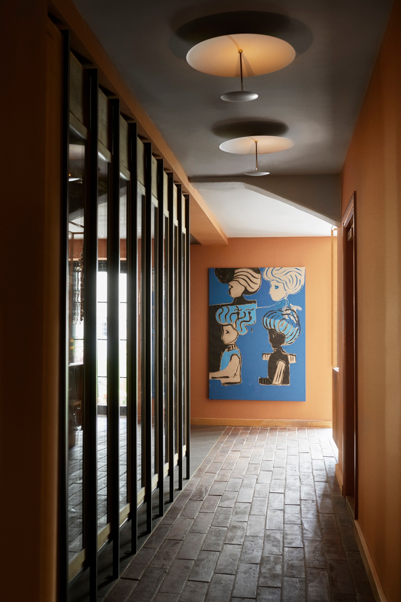 Hallway with vertical black slats, warm lighting, stone floor and colorful artwork on peach wall