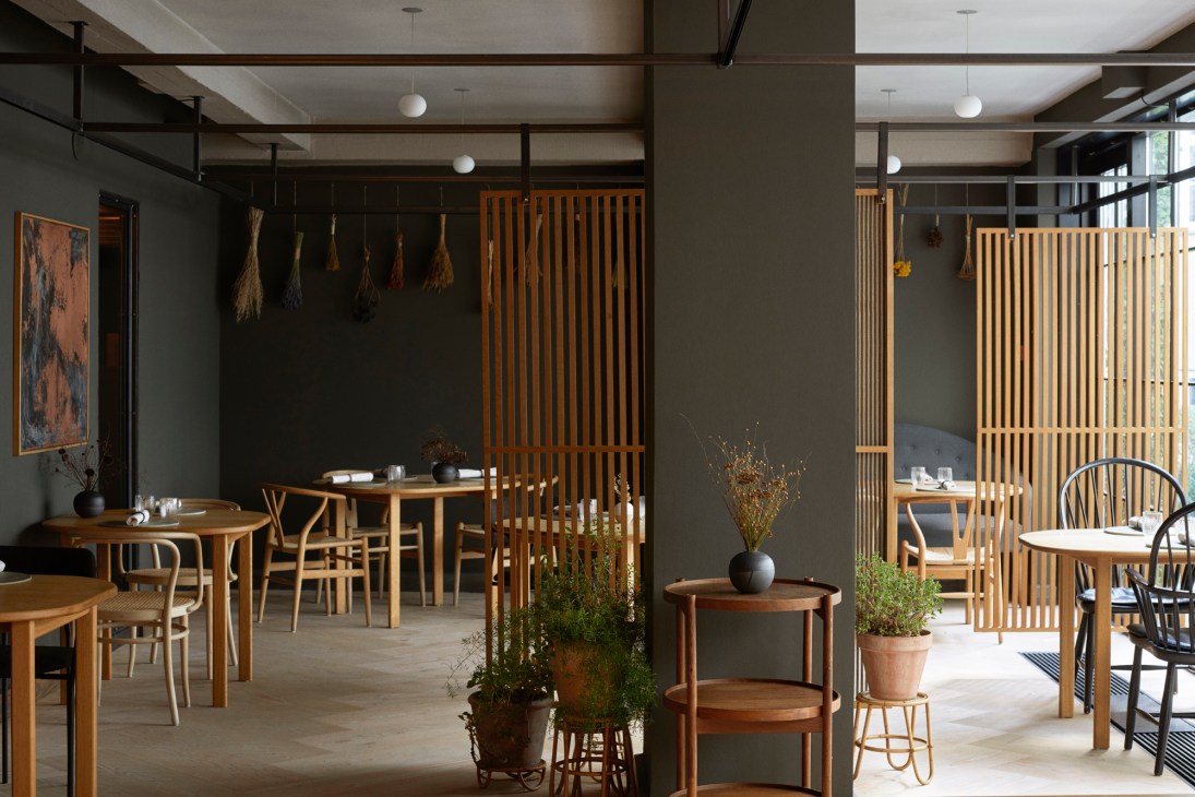 Restaurant dining room with wooden furniture, vertical wood slat partitions, and plants creating intimate seating areas