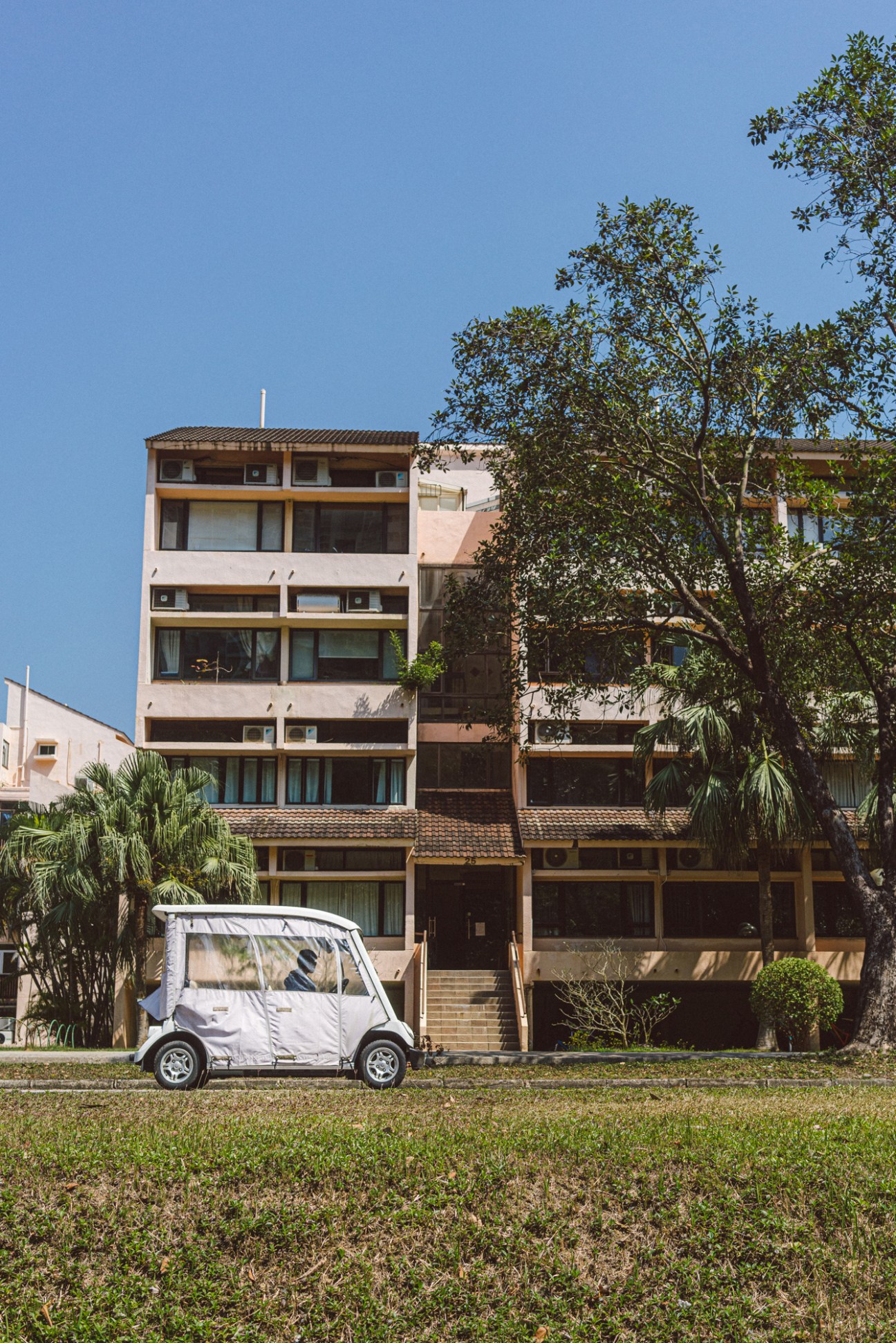 White golf cart parked on grass in front of modern residential buildings with palm trees