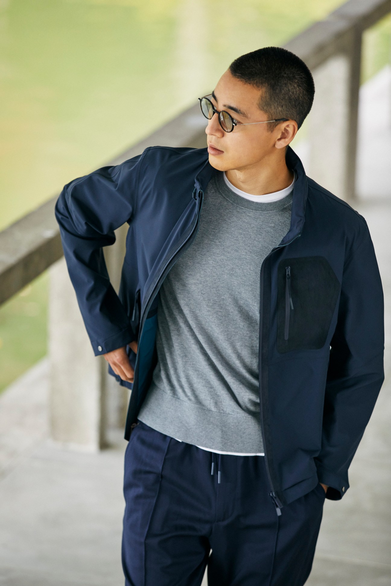 Young Asian man in navy jacket, grey sweater and sweatpants looking to the side wearing glasses