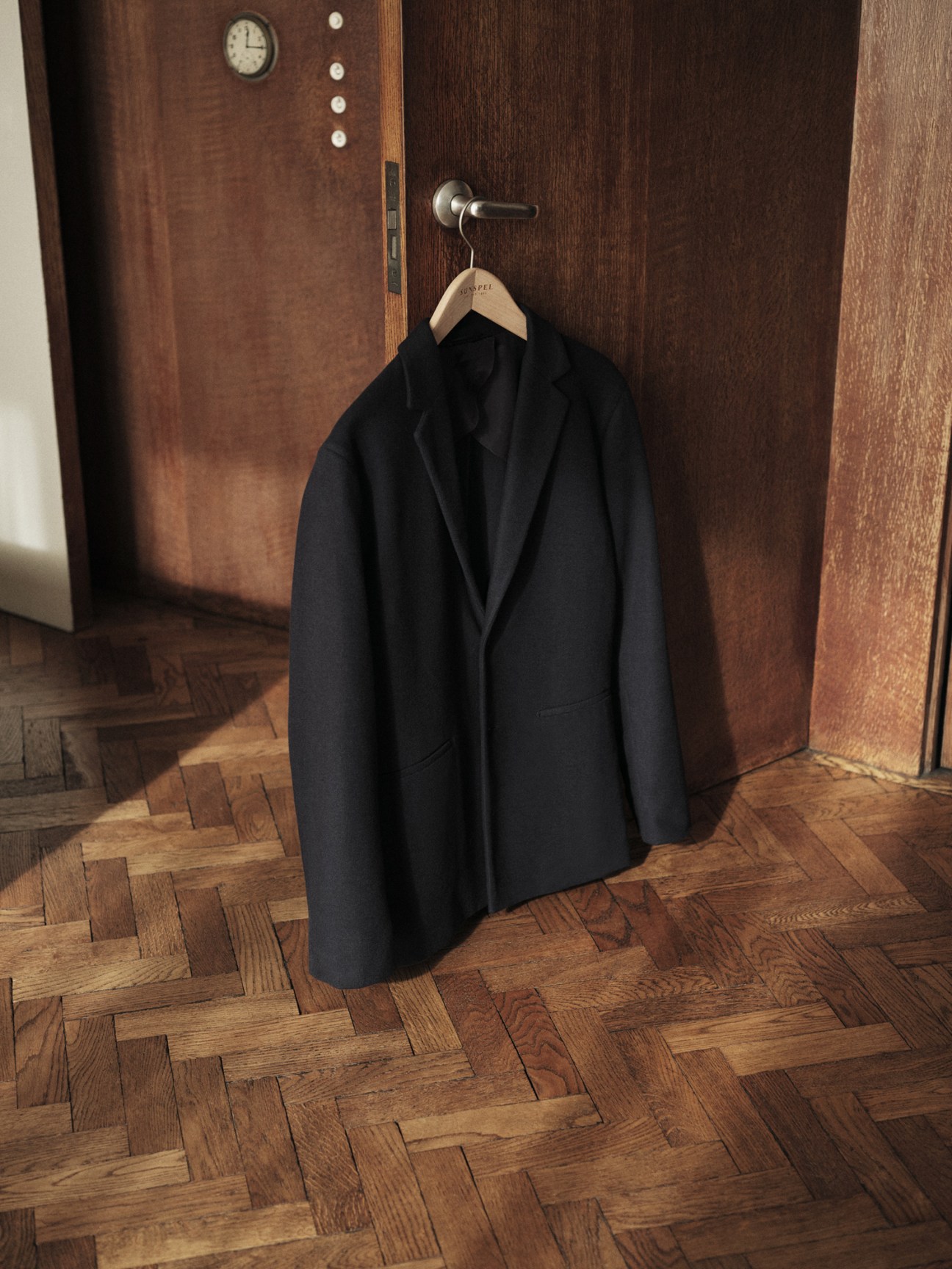 Dark navy suit jacket hanging on wooden coat hanger against wood paneled door