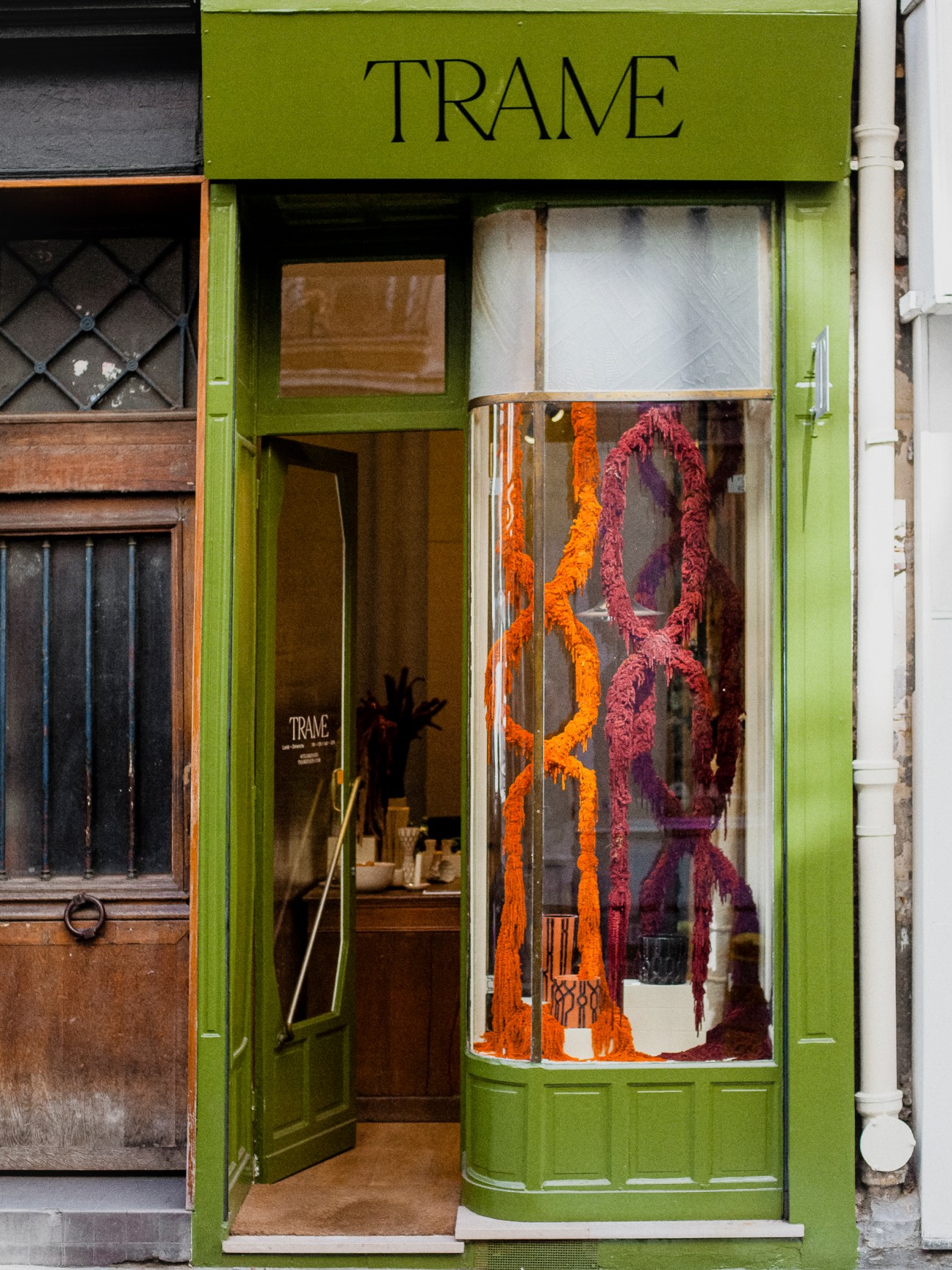 Green storefront of Trame shop in Le Marais with art deco facade and colorful yarn installation in window