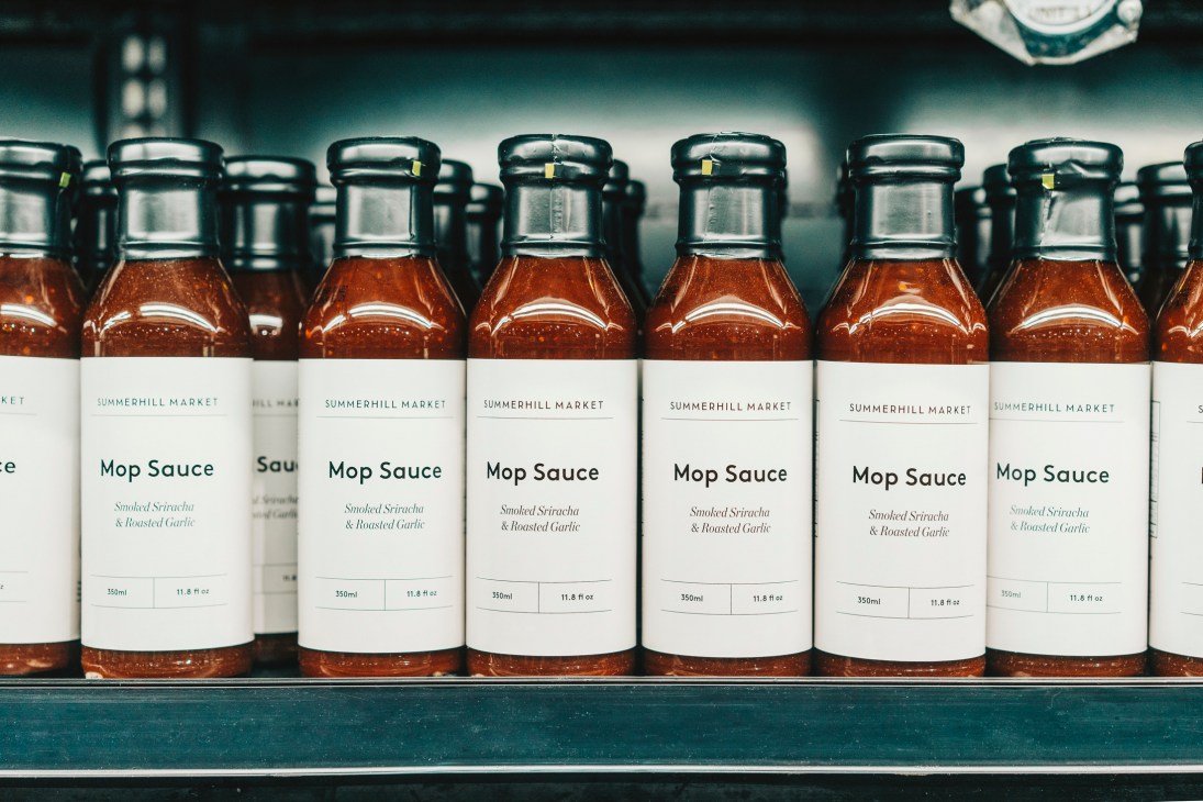 Rows of glass bottles with amber-colored sauce and white labels displaying Summerhill Market branding on store shelf
