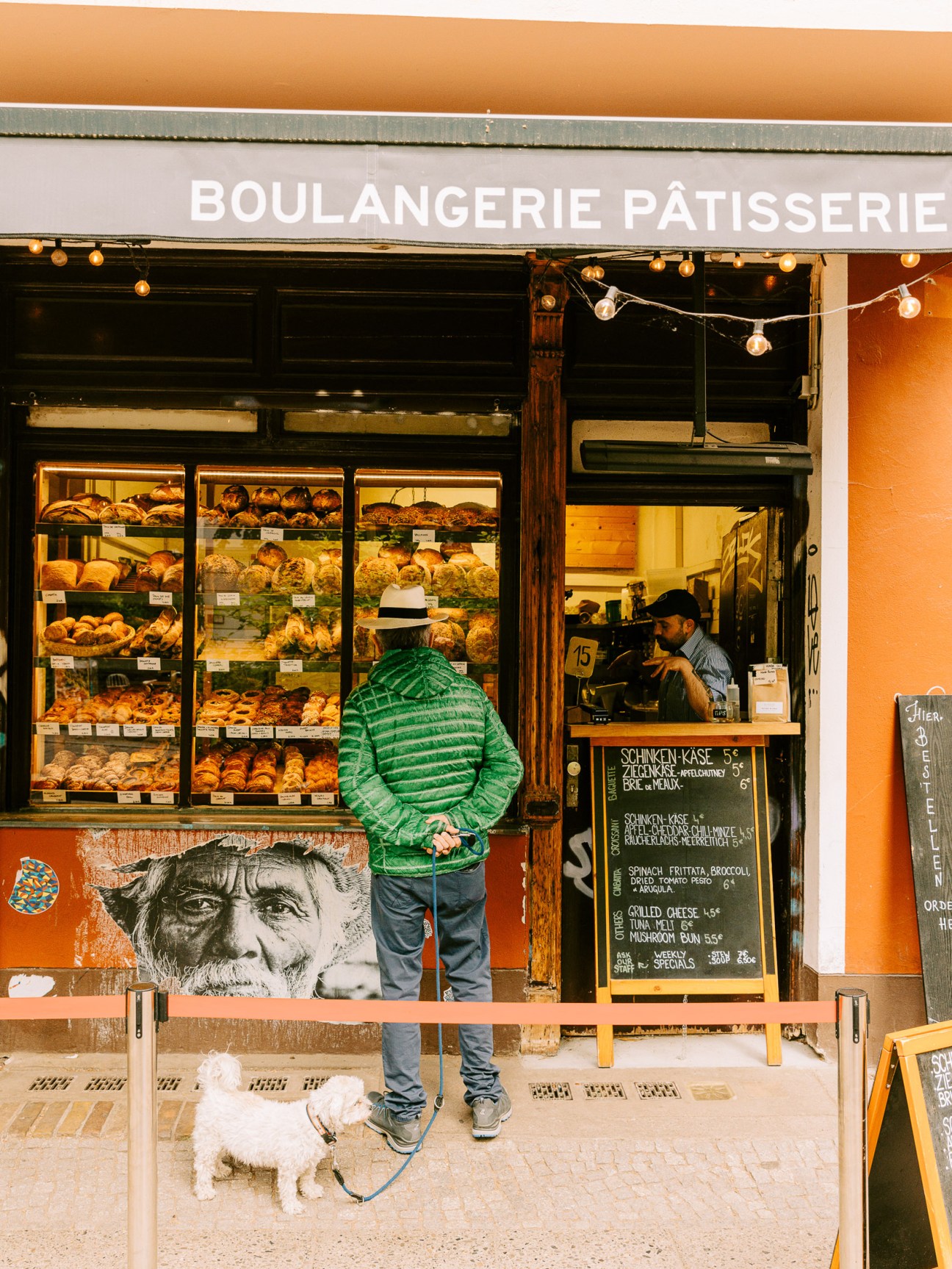 Customer in green striped jacket browsing pastries at a boulangerie patisserie storefront with display cases