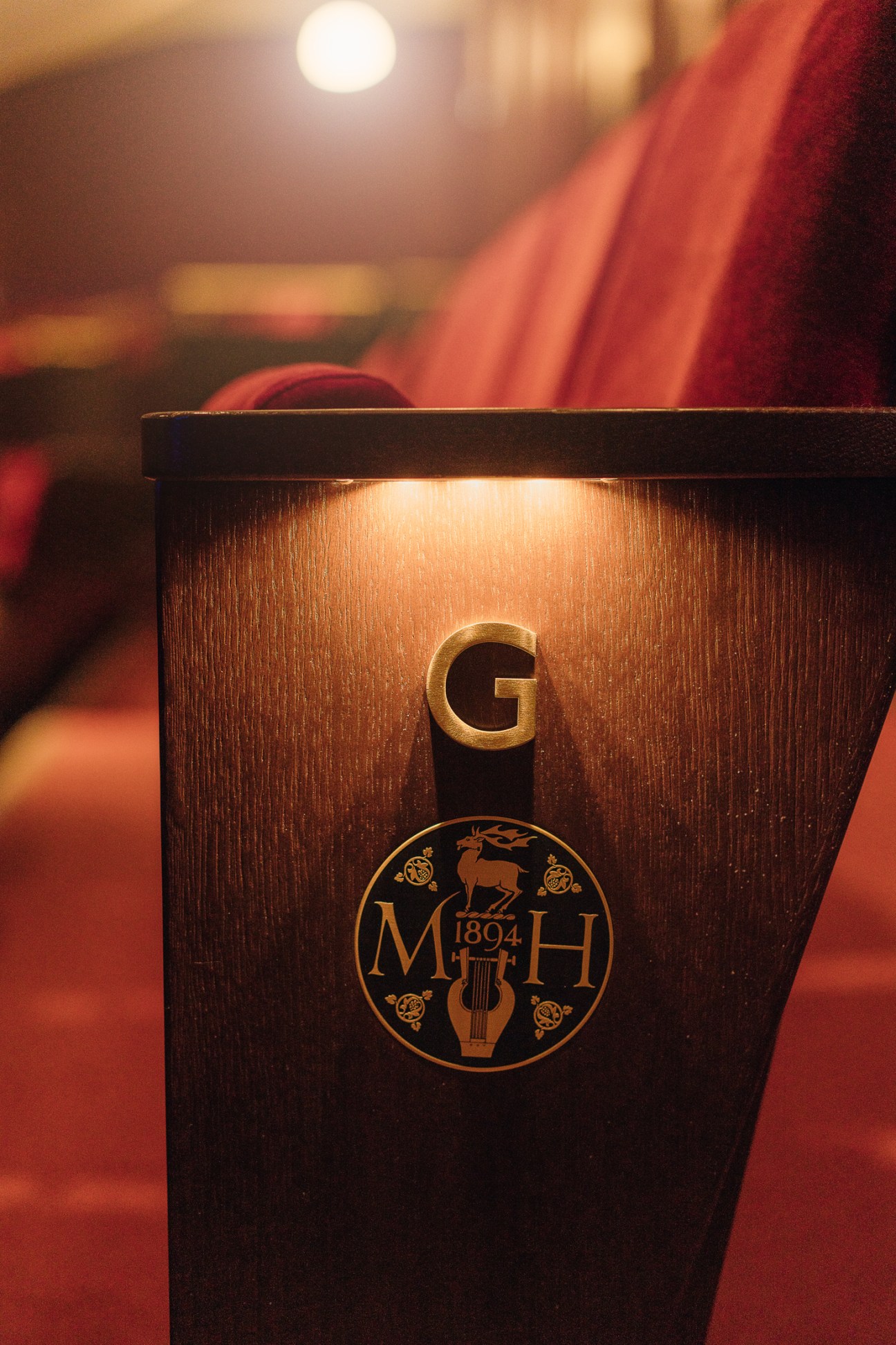 Gold letter G and circular MH 1894 logo on dark wood surface at Massey Hall