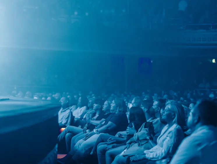 Audience members seated in rows at Massey Hall watching a performance with dramatic blue stage lighting