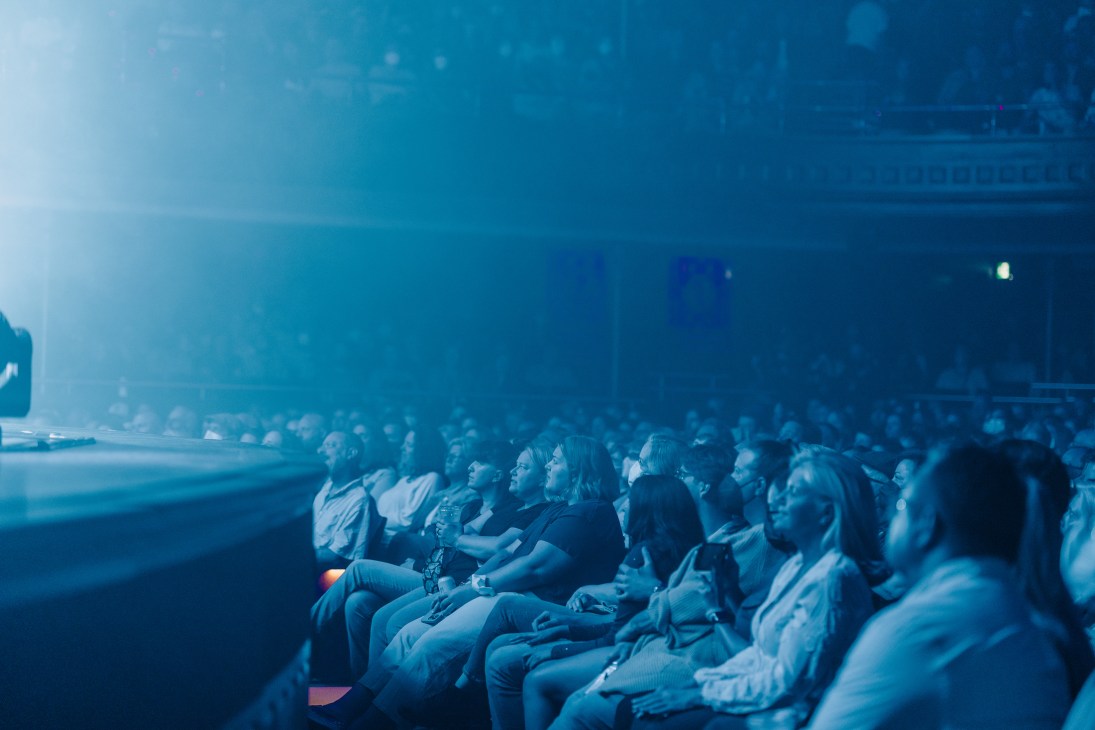 Audience members seated in rows at Massey Hall watching a performance with dramatic blue stage lighting