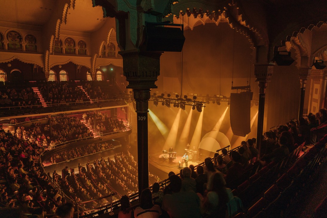 Interior view of packed Massey Hall auditorium with ornate architecture, multiple balcony levels, and stage lighting