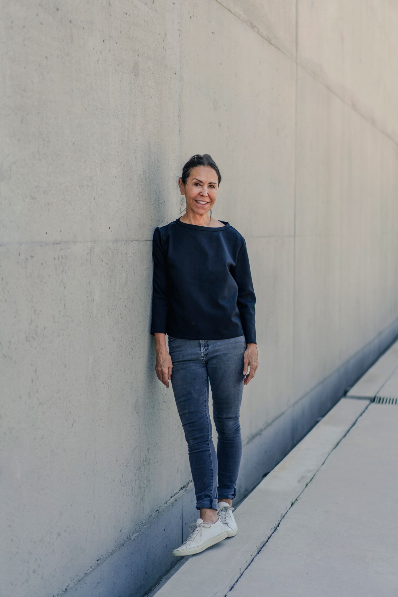 Pat Hanson standing against a concrete wall wearing a dark sweater and jeans