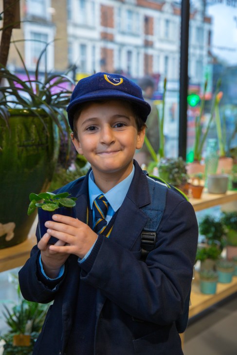 Young boy in school uniform holding a potted plant inside The Nunhead Gardener garden centre.