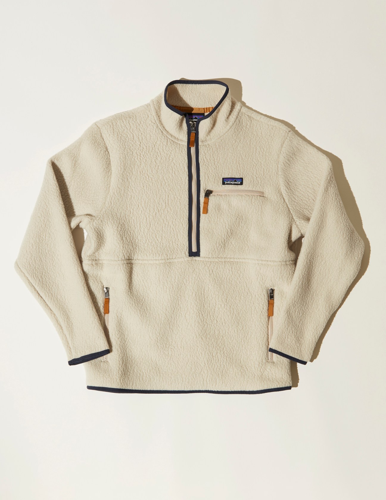 Cream colored Patagonia fleece pullover with navy trim and orange zipper pulls on white background