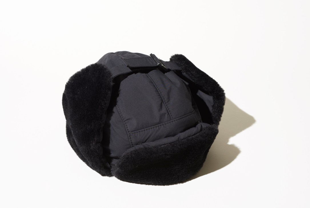 Black winter hat with fur-lined ear flaps and ties, photographed against white background
