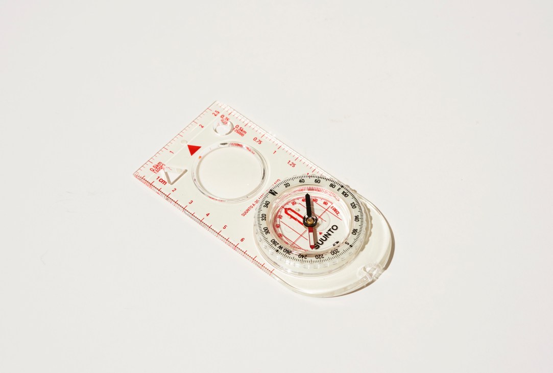 A clear plastic compass with red markings, measurement ruler, and circular dial showing directional readings