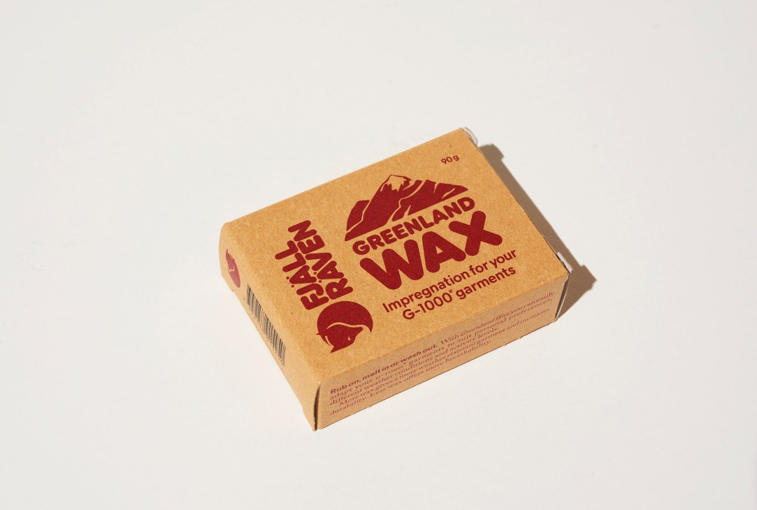 Orange cardboard box of Fjällräven Greenland wax for garment waterproofing on white background