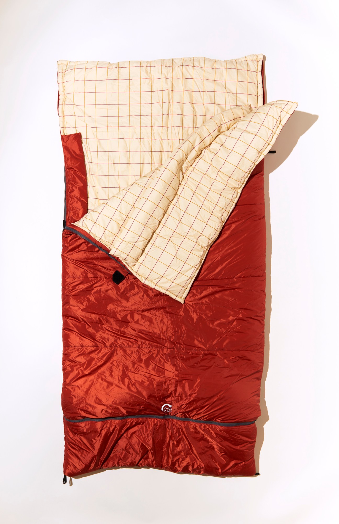 Red outdoor sleeping bag with cream checkered interior lining partially unzipped and opened