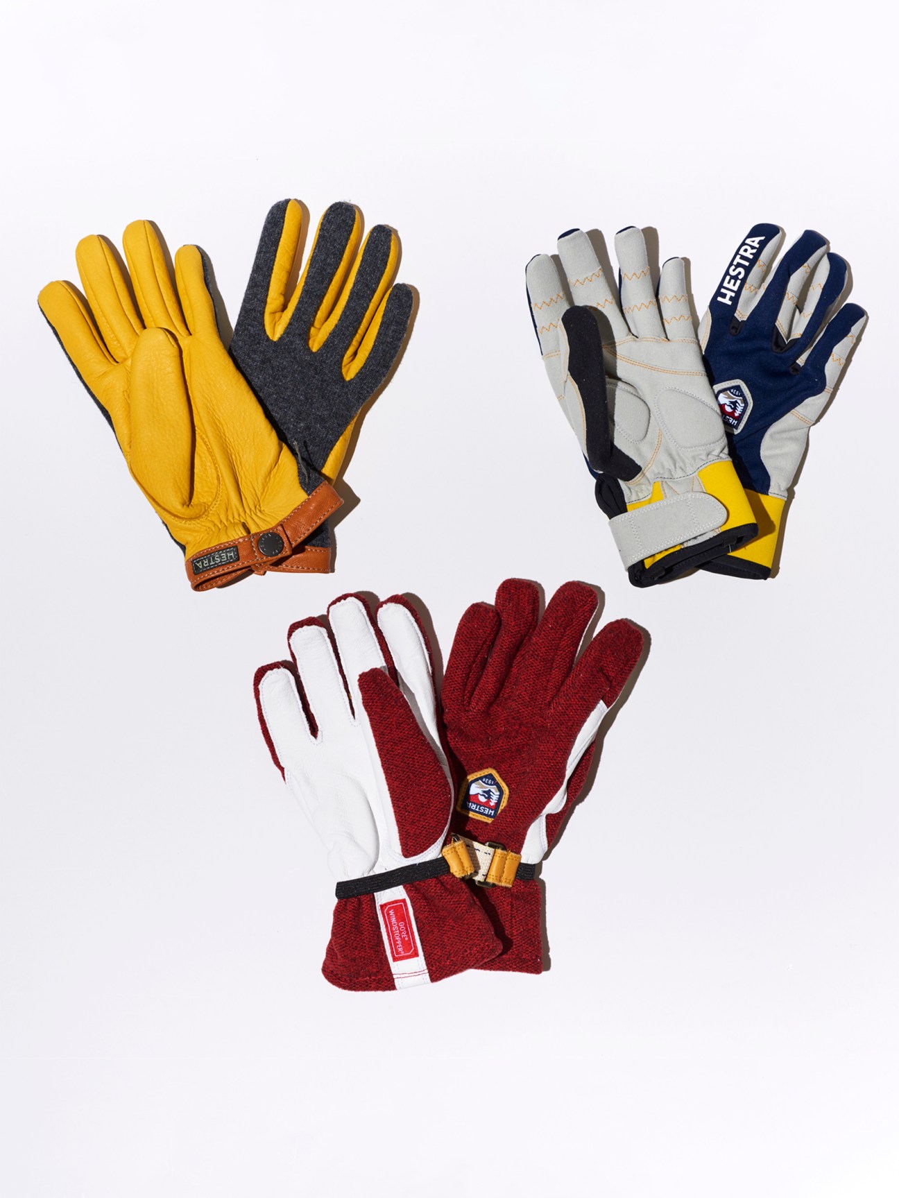 Three pairs of outdoor gloves in yellow, navy/white, and red/white colorways arranged on white background