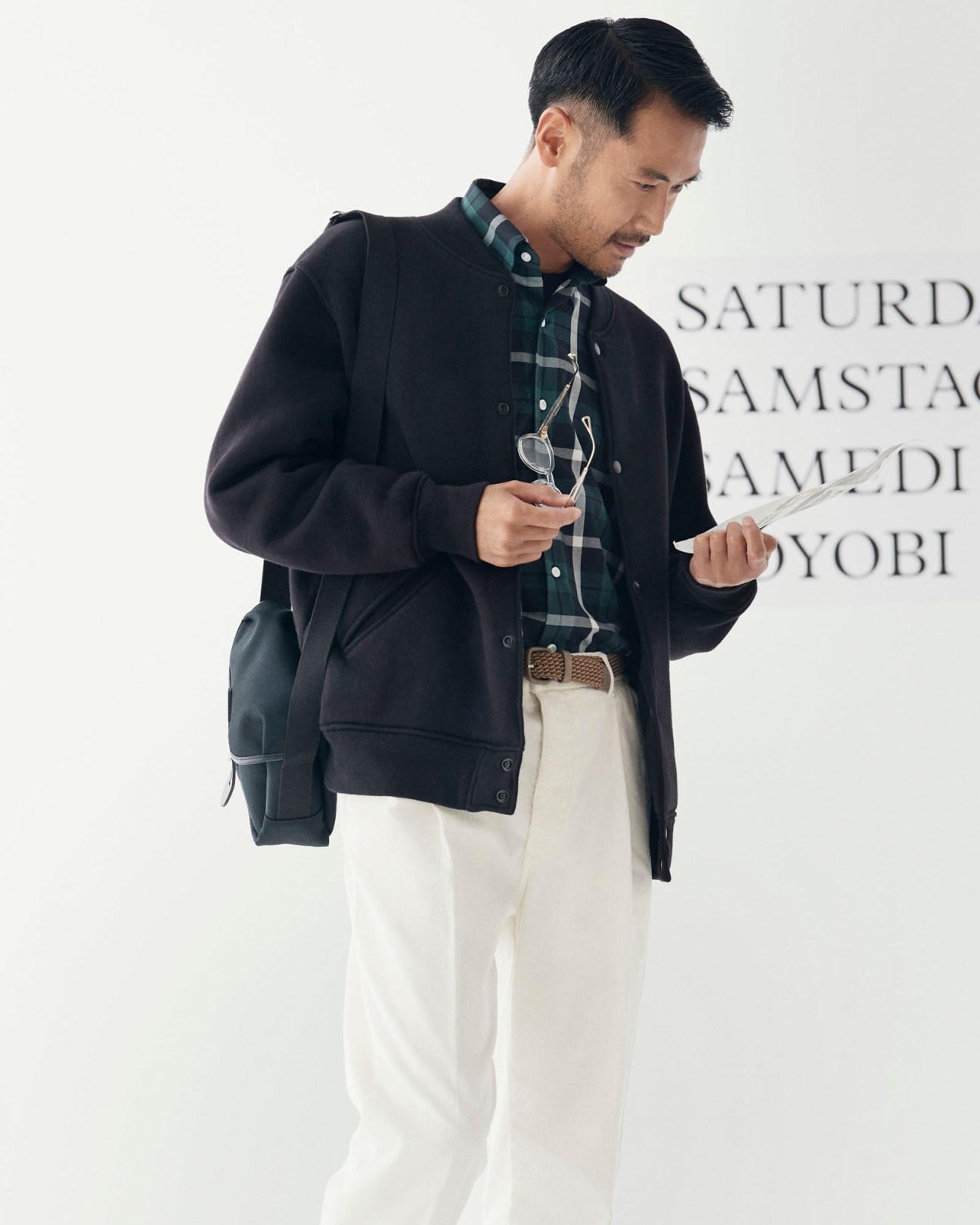 Model wearing beige jacket, striped shirt, white t-shirt, cream trousers, holding glasses and papers
