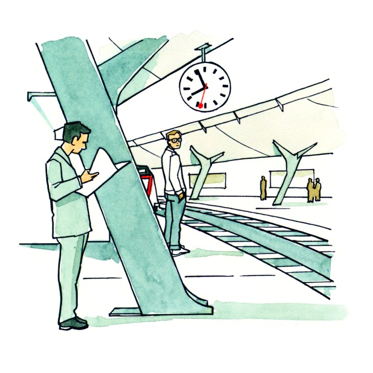 People waiting at a train station platform with a large Mobatime clock showing the time overhead