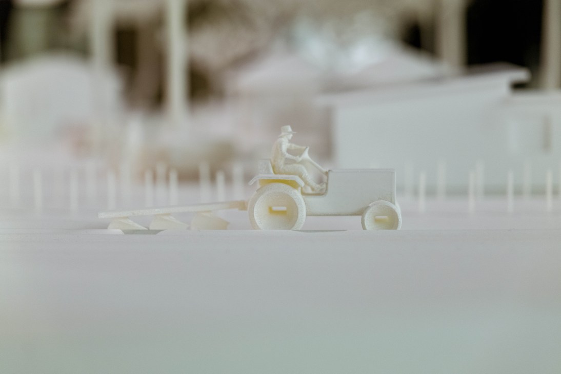 White sculptural electric tractor model on white display surface in museum exhibition space