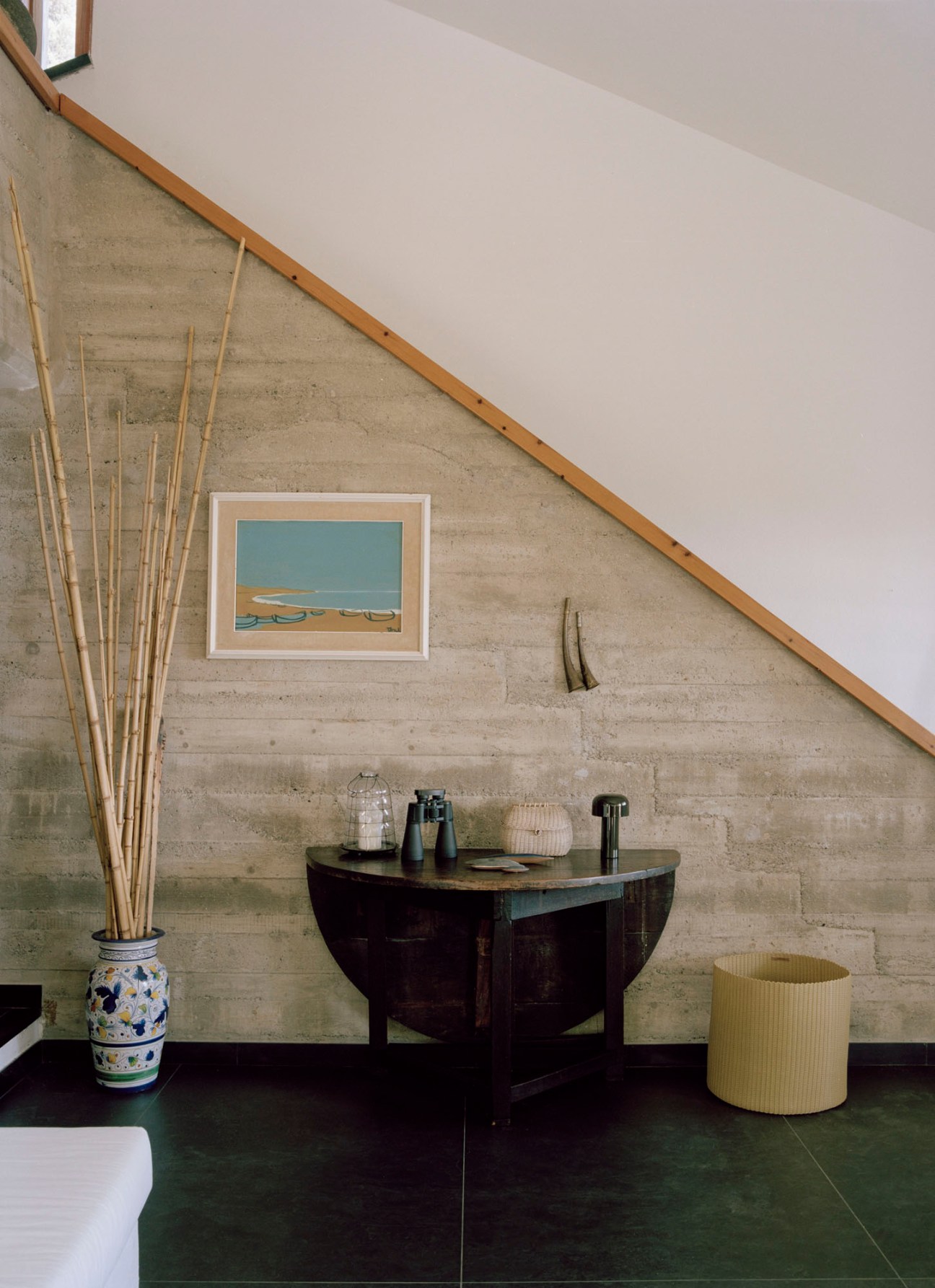 Interior space with concrete walls, dark round table, decorative vase with bamboo sticks, and wicker basket