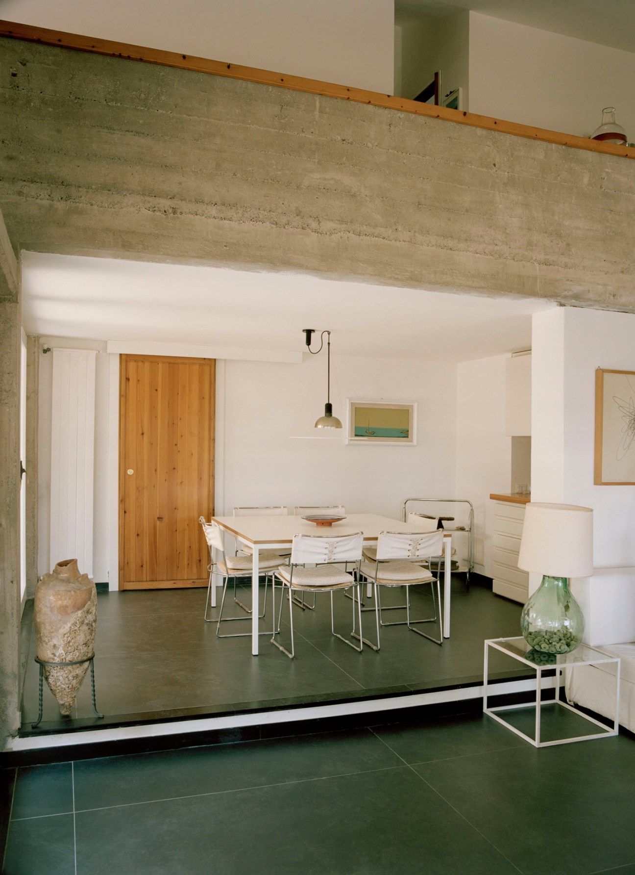 Modern dining room with white table, metal chairs, concrete ceiling beam, green floors and wooden door