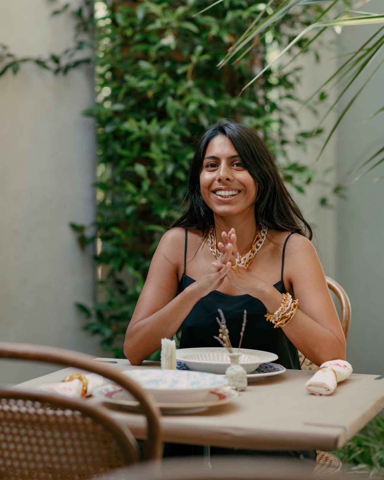 Rosh Mahtani, founder of Alighieri jewellery, smiling at a table with white plates and golden jewelry