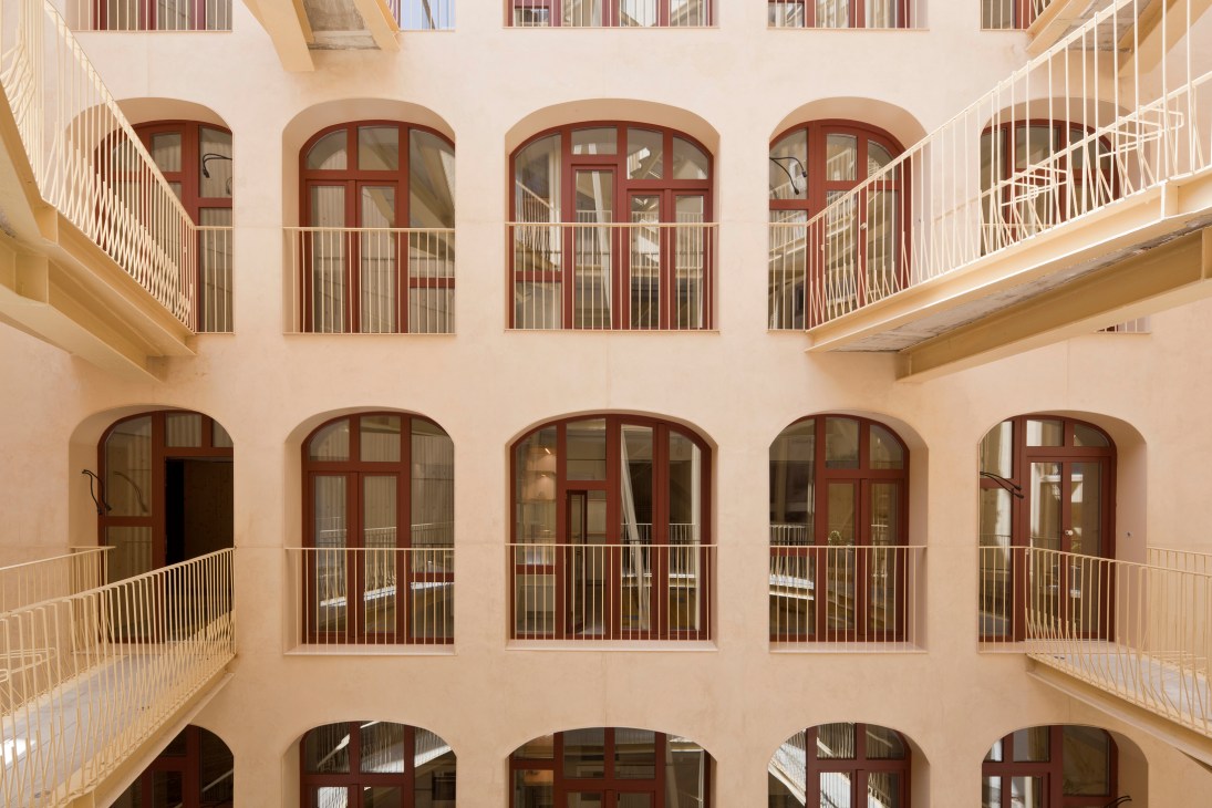 Interior courtyard of La Carbonería building showing multiple levels of arched windows with red frames and white railings