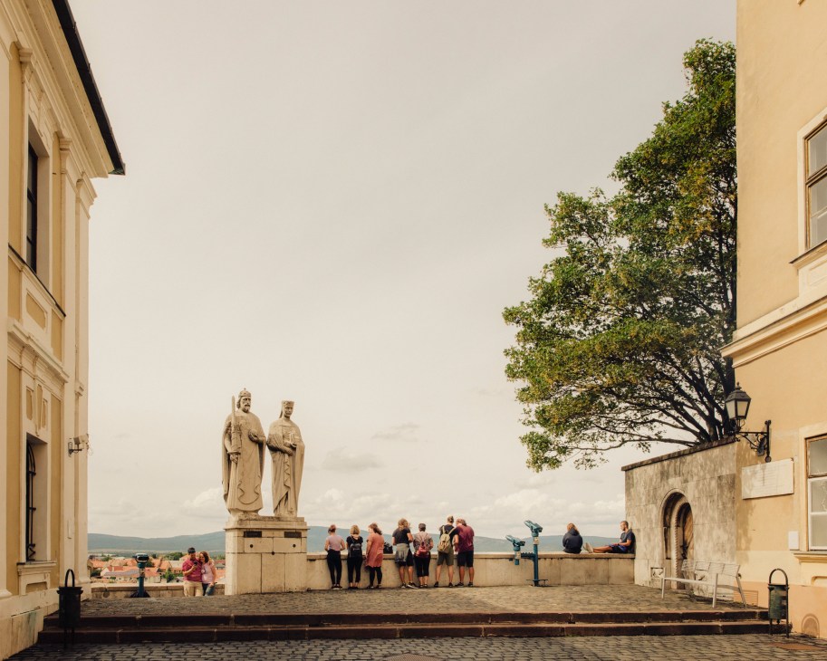 Stone statue of two figures on cobblestone square with tourists viewing cityscape from Veszprem overlook