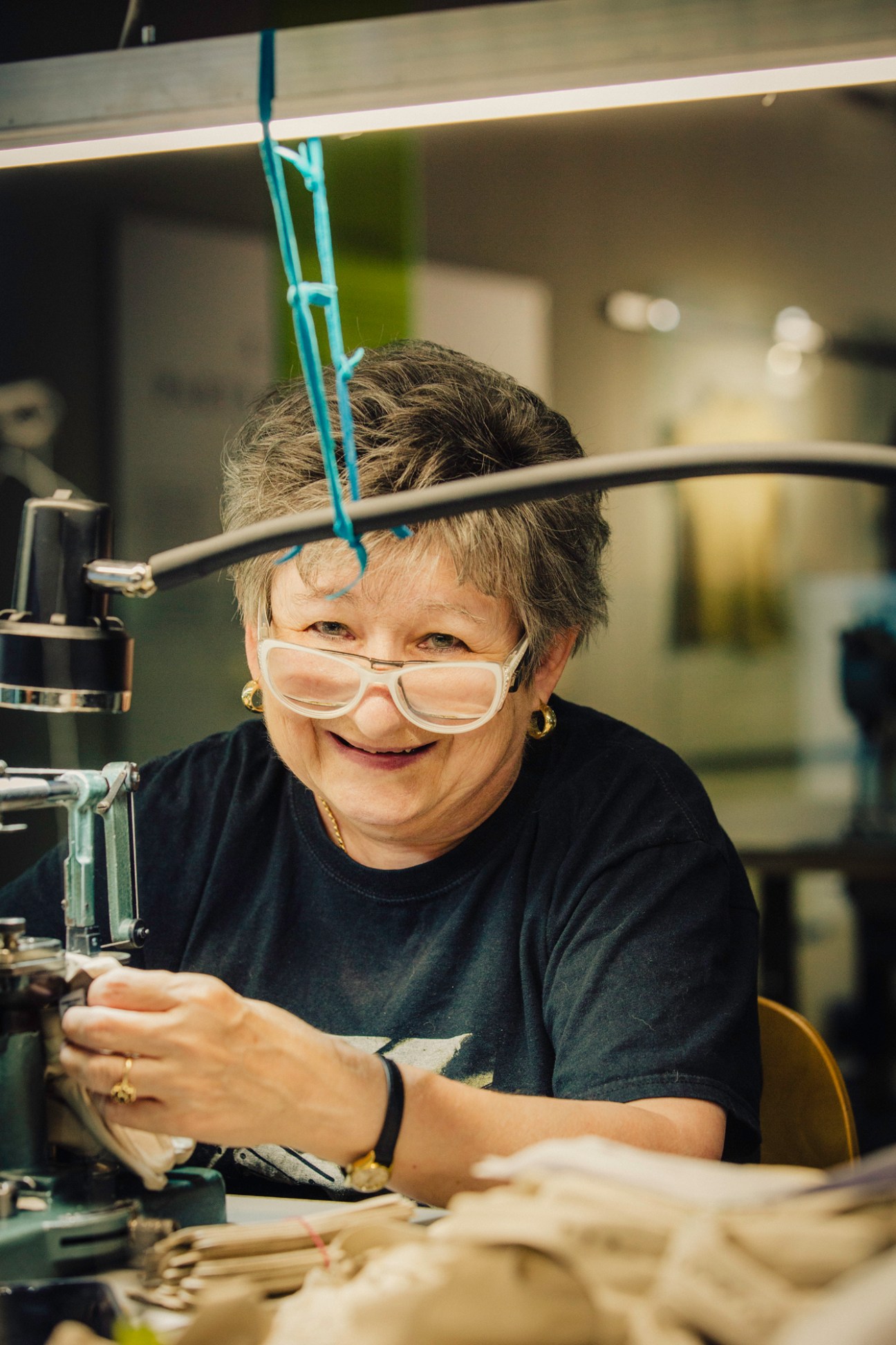 Elderly woman working at sewing machine at Hamerli glove factory wearing protective glasses