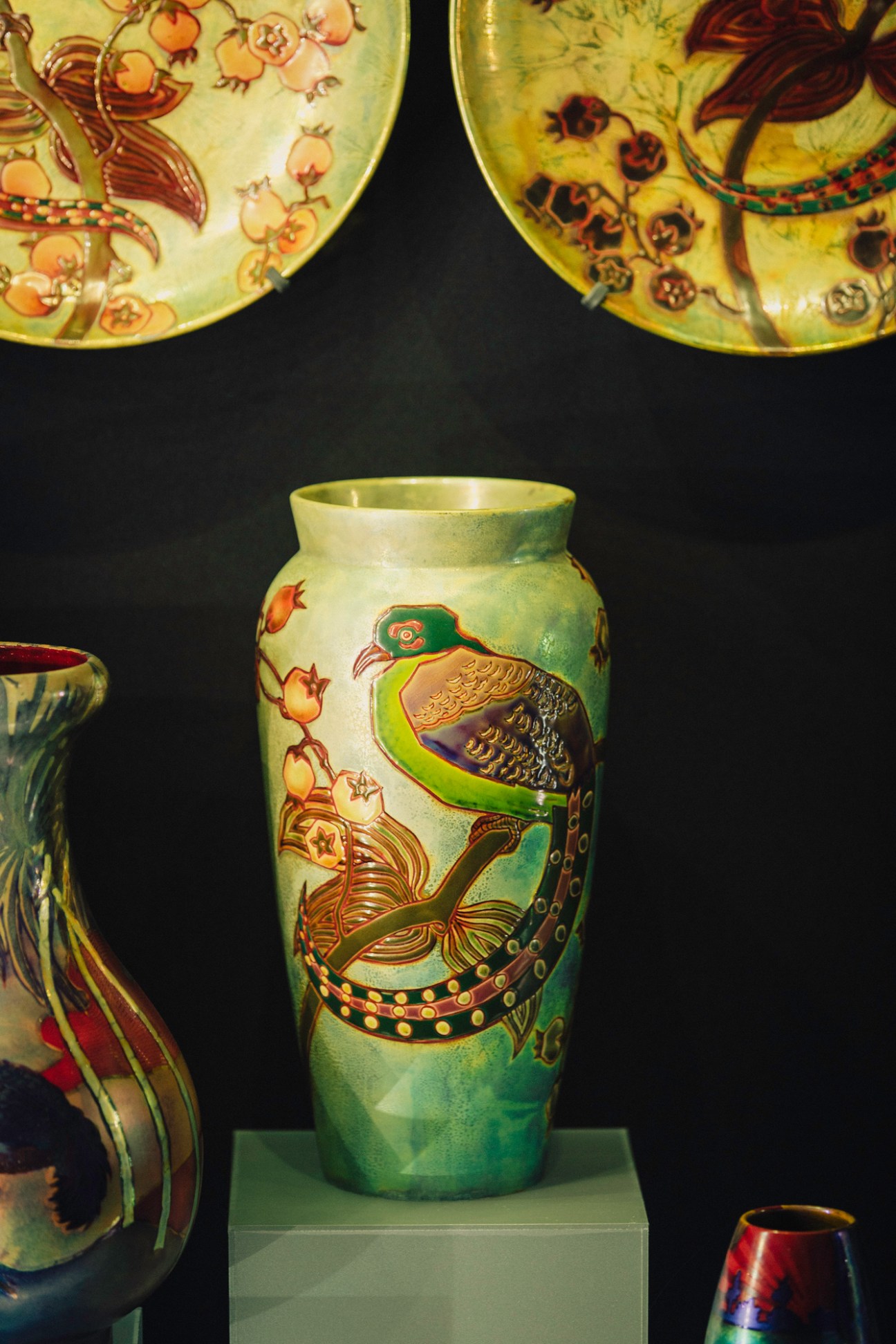 Ornate Zsolnay porcelain vase with colorful bird and floral motifs displayed alongside decorative plates