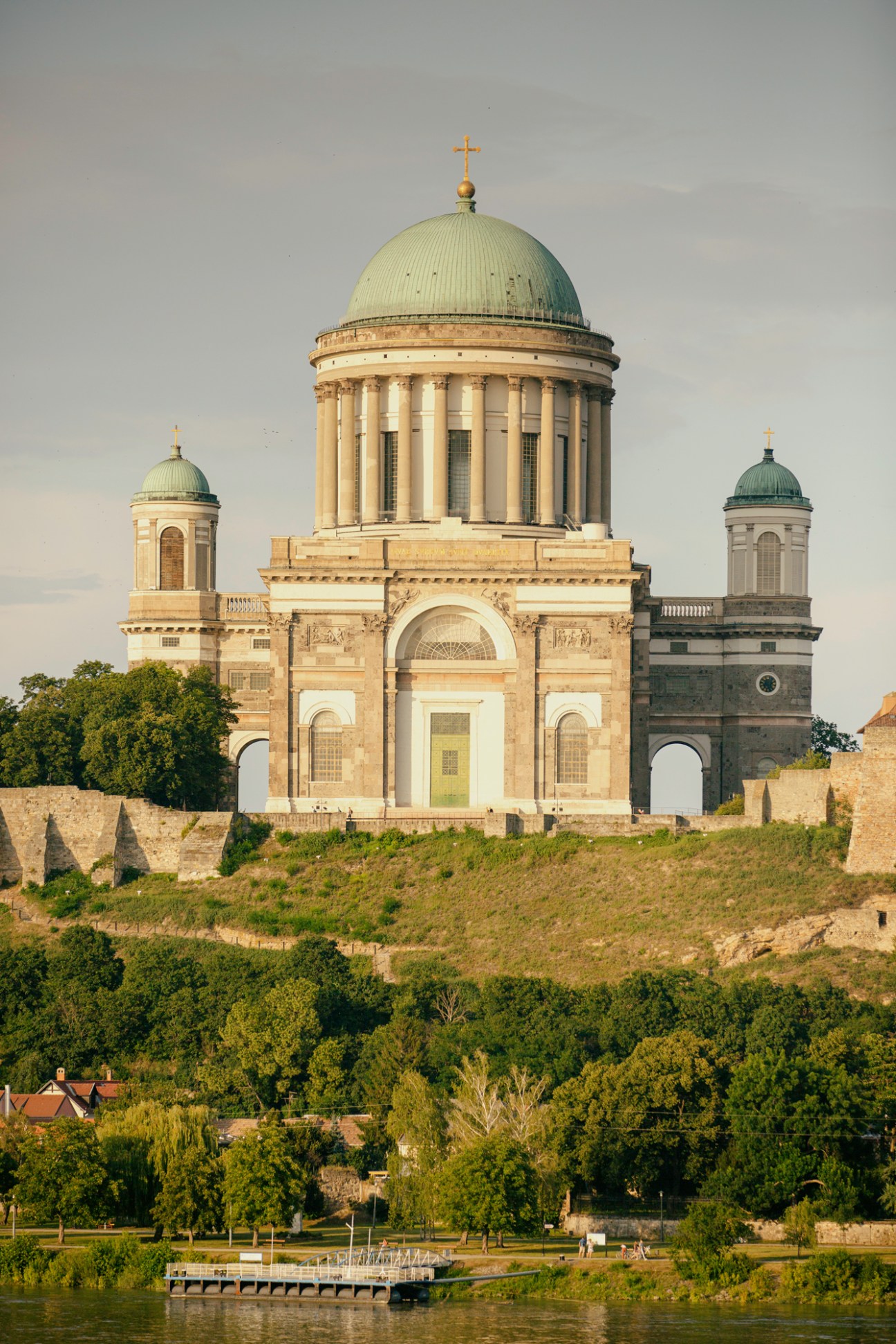 Esztergom Basilica with its distinctive green copper dome and neoclassical columned structure on a hillside above the Danube River in Hungary.