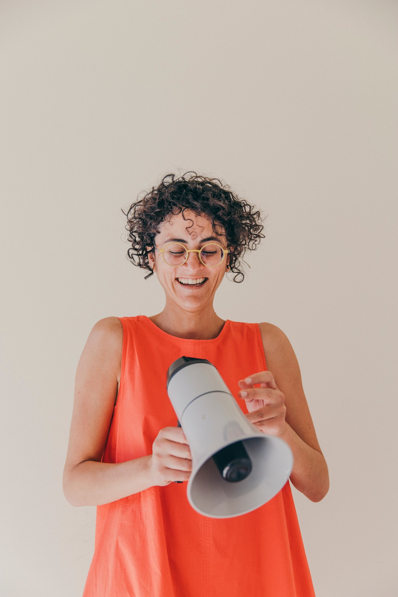 Person in orange tank top holding white and black megaphone while smiling