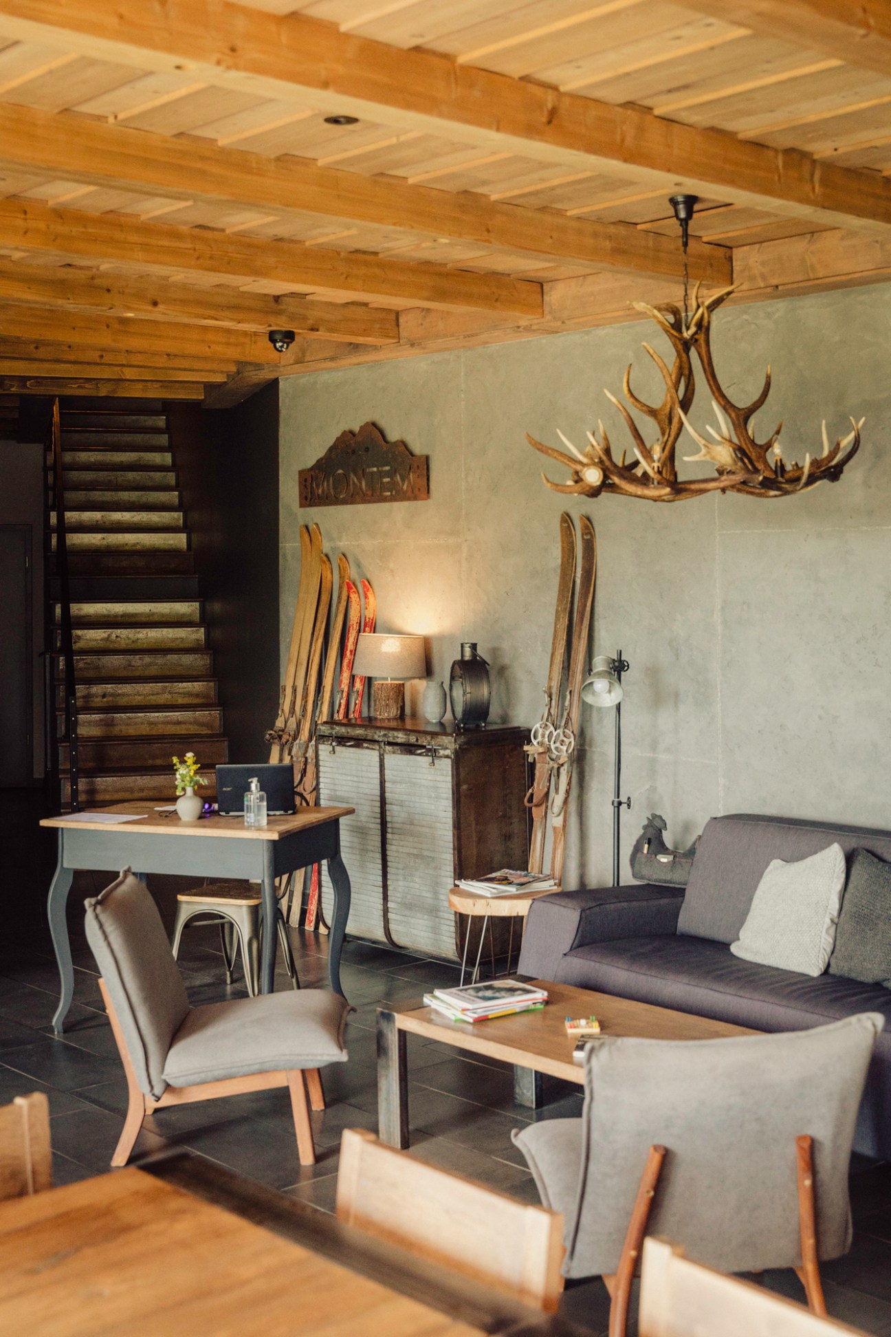 Rustic mountain hotel room with exposed wooden ceiling beams, antler chandelier, and vintage skiing equipment