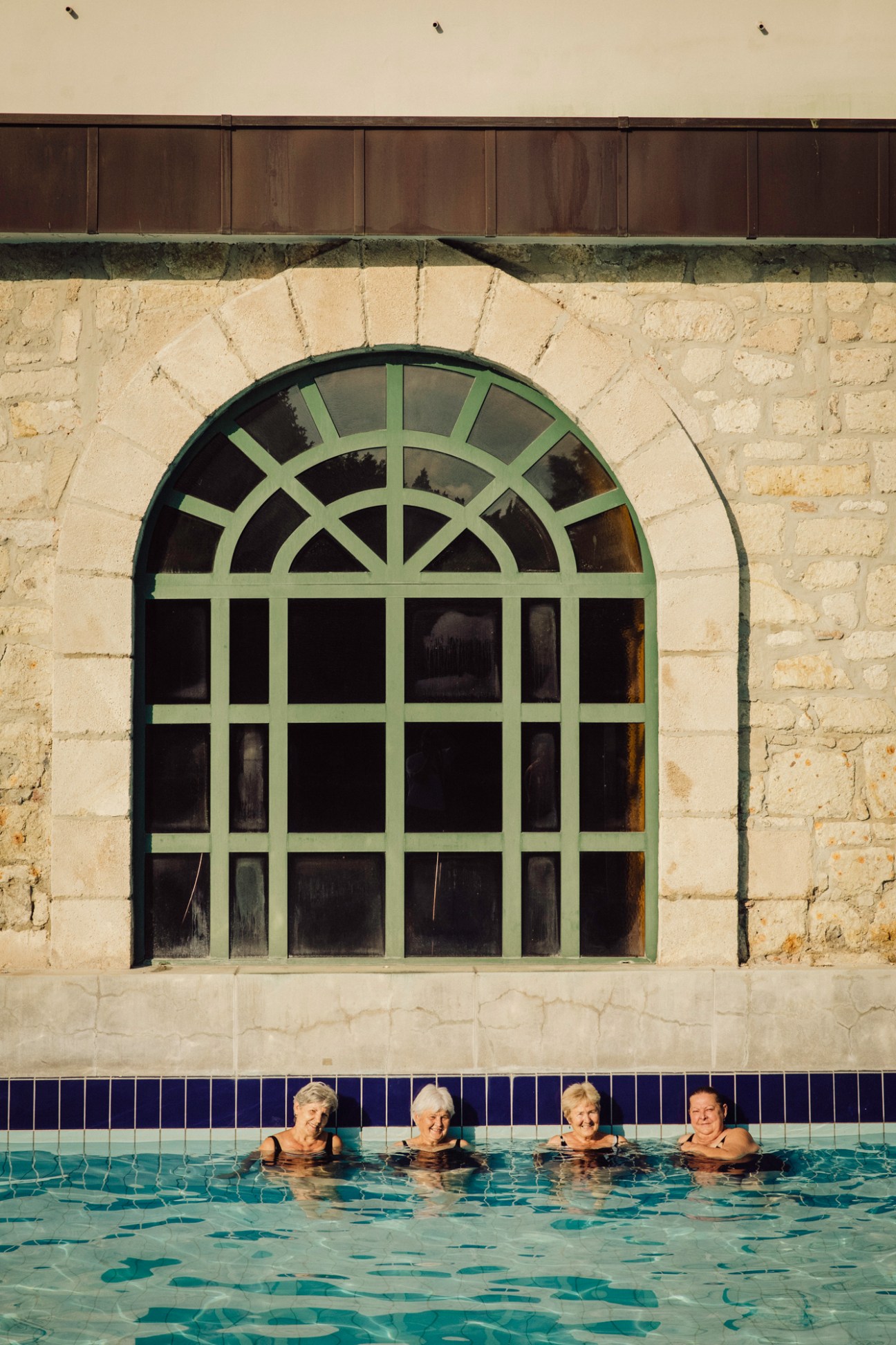 Four people relaxing in thermal pool at Turkish bath with ornate arched window and stone architecture